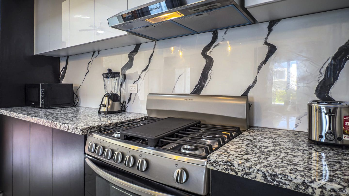 buyDRproperty Modern kitchen with stainless steel appliances, granite countertops, and marble-look backsplash. Sosua Real Estate