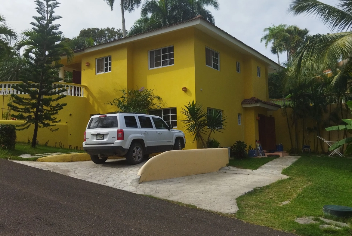 buyDRproperty Charming yellow villa with white Jeep parked in the driveway. Lush landscaping. Sosua Real Estate