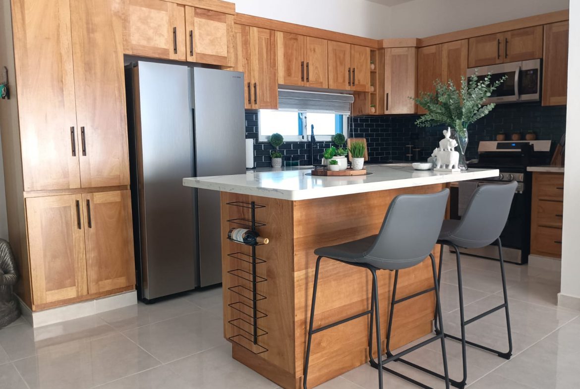 buyDRproperty Modern kitchen with wooden cabinets and island, featuring bar stools and wine rack. Sosua Real Estate