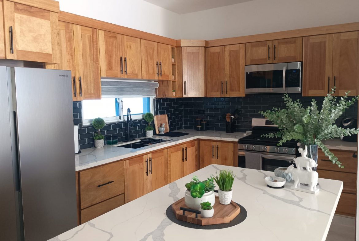 buyDRproperty Modern kitchen with light wood cabinets, black backsplash, and white countertop. Sosua Real Estate