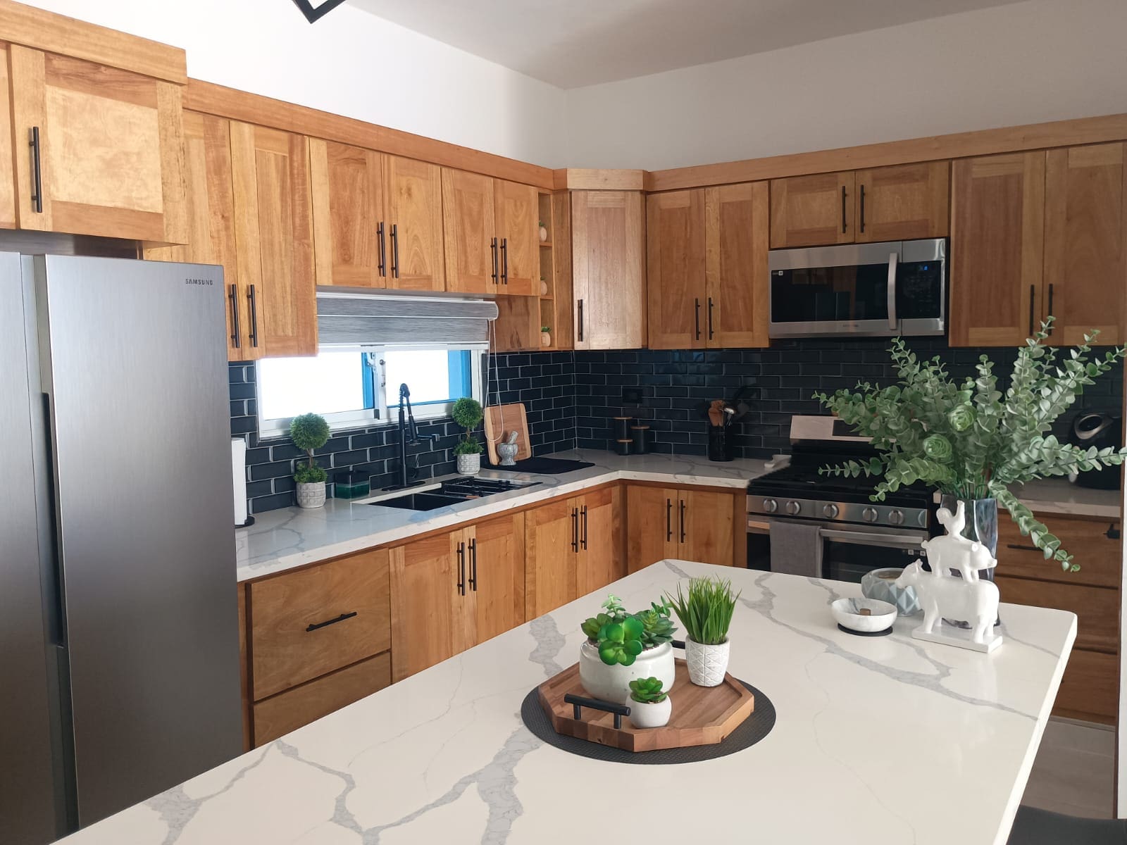 buyDRproperty Modern kitchen with light wood cabinets, black backsplash, and white countertop. Sosua Real Estate