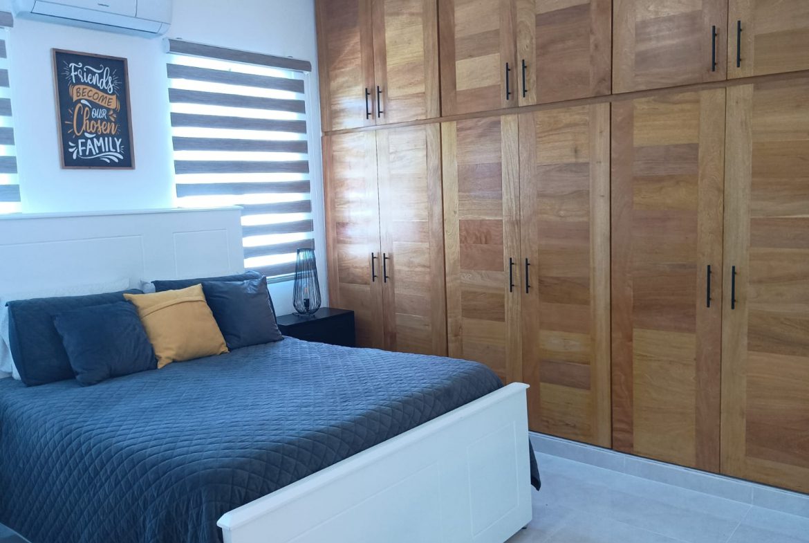 buyDRproperty Modern bedroom with large wooden wardrobes and a bed with blue bedding. Sosua Real Estate