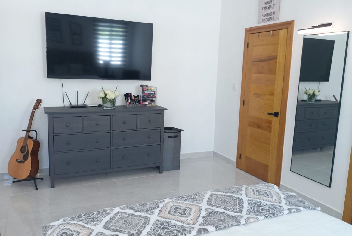 buyDRproperty Modern bedroom with gray dresser, TV, and guitar in a Puerto Plata villa. Sosua Real Estate