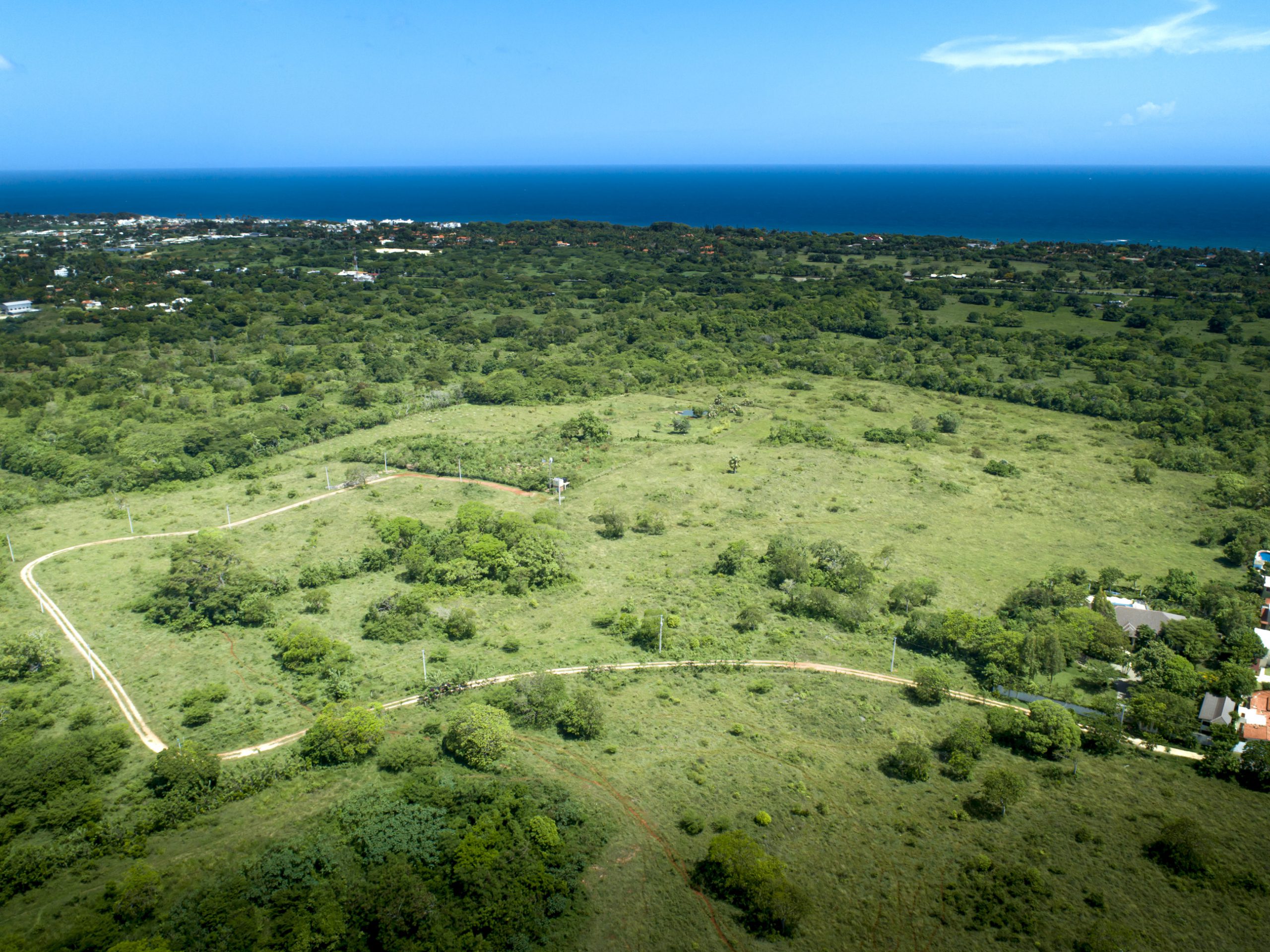 buyDRproperty Aerial view of lush green landscape with winding road, trees, and ocean in the distance. Sosua Real Estate