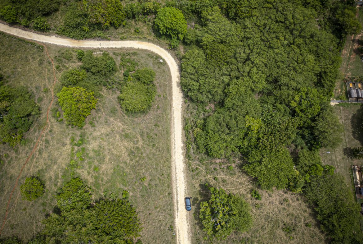 buyDRproperty Aerial view of a dirt road winding through lush green nature trails, captured by drone photography. Sosua Real Estate