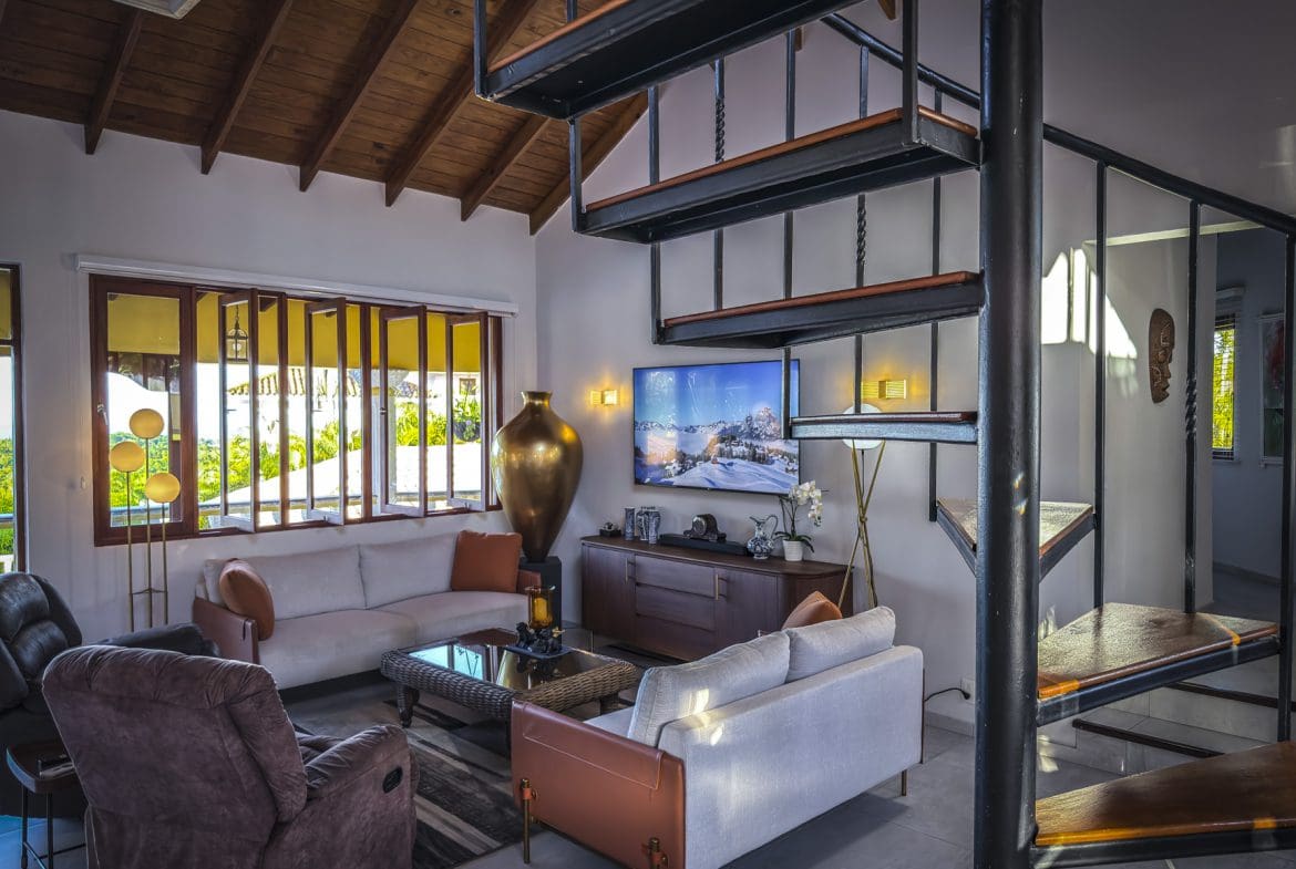 buyDRproperty Living room in a luxury villa for sale with ocean views, featuring a spiral staircase and modern decor. Sosua Real Estate