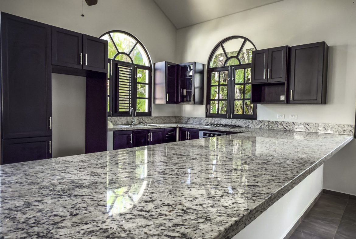 buyDRproperty Modern kitchen with dark cabinets, granite countertops, and arched windows Sosua Real Estate