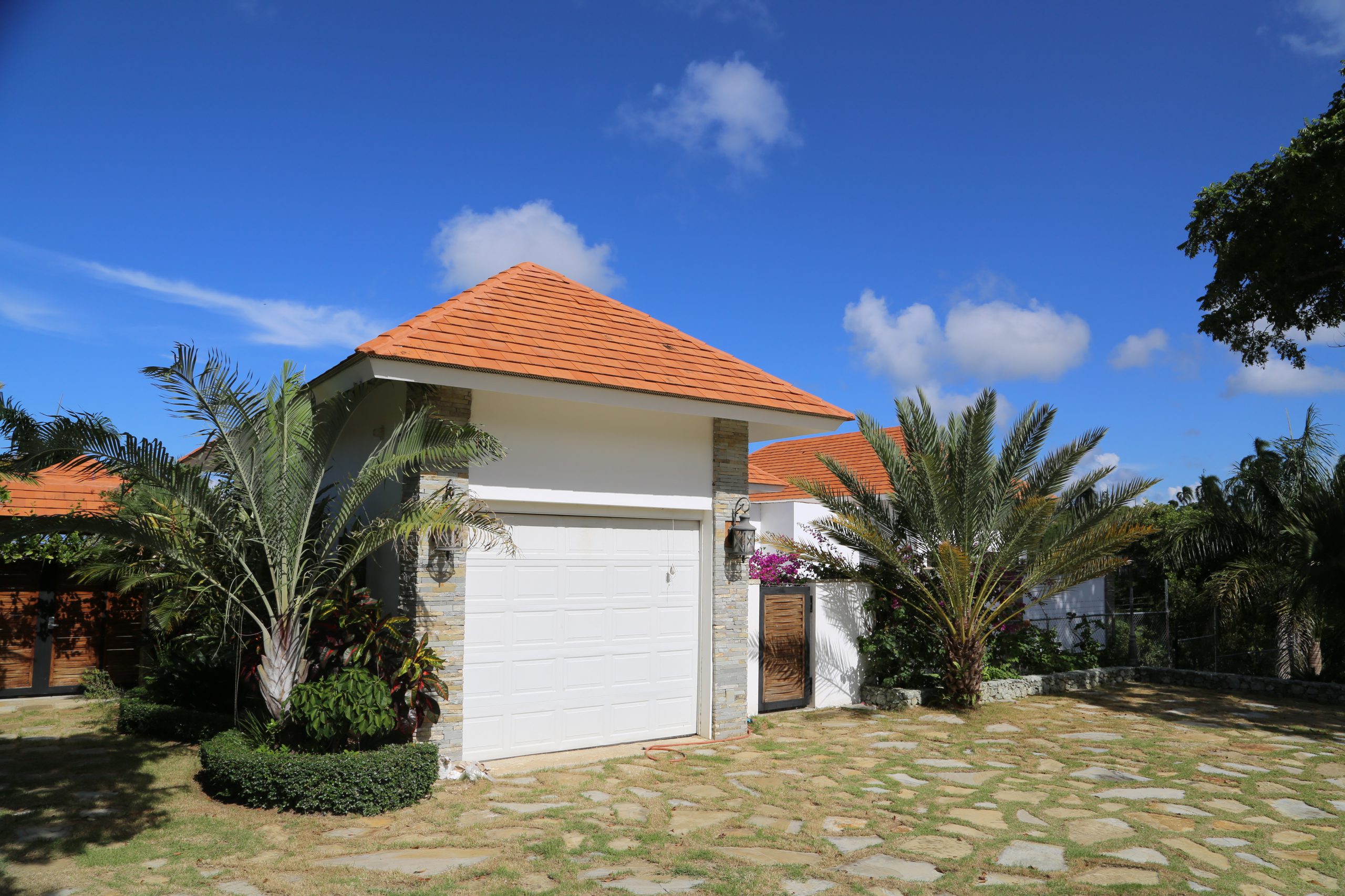 buyDRproperty Small house with orange roof, surrounded by palm trees under a clear blue sky Sosua Real Estate