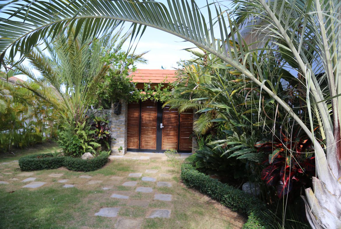 buyDRproperty Tropical garden pathway leading to a wooden door surrounded by lush greenery Sosua Real Estate