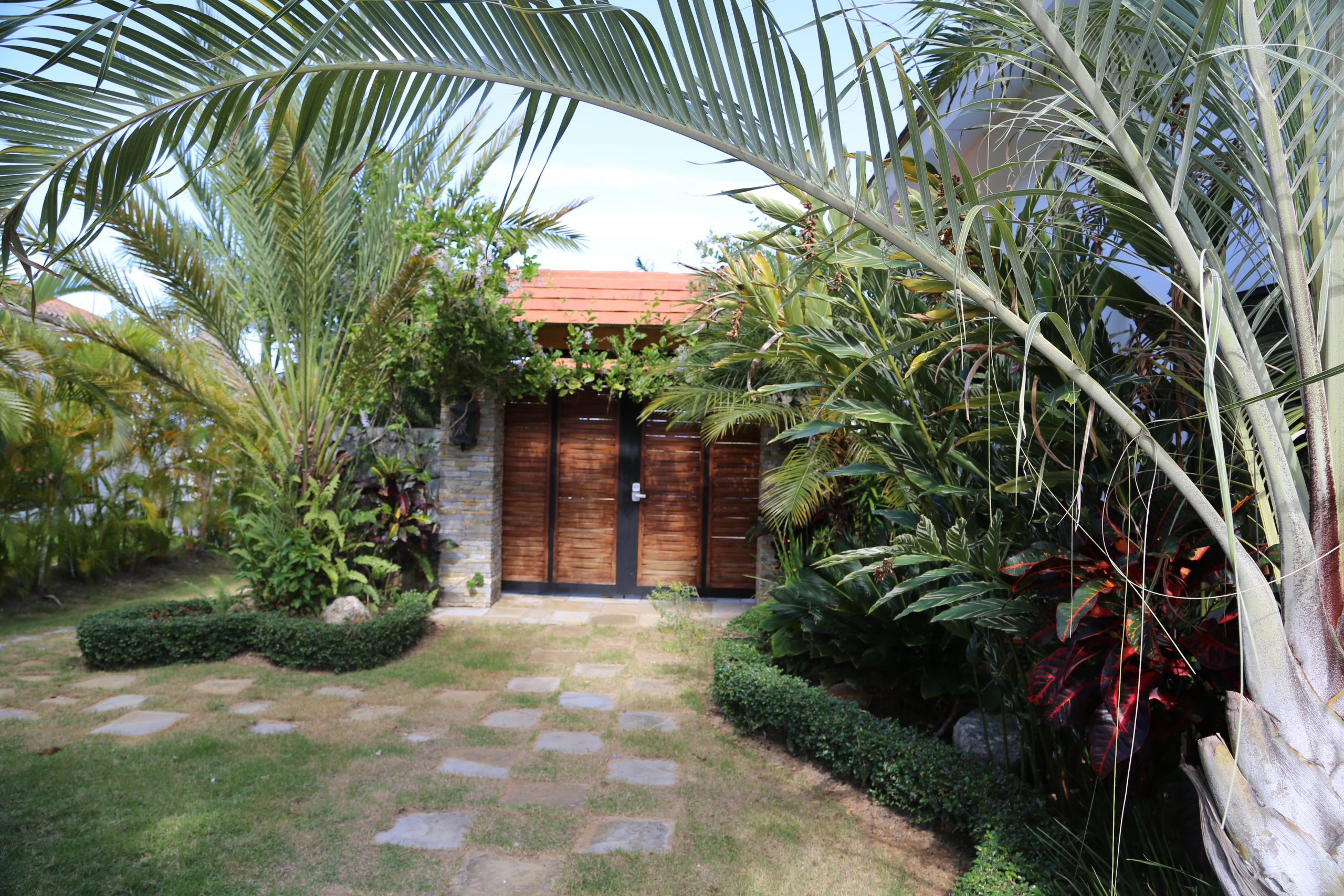 buyDRproperty Tropical garden pathway leading to a wooden door surrounded by lush greenery Sosua Real Estate