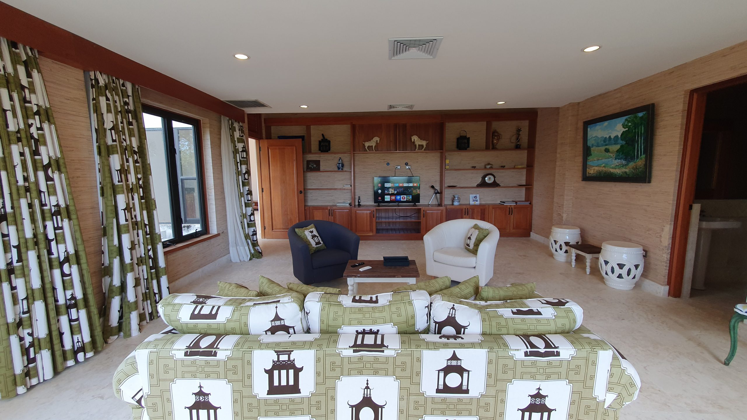 buyDRproperty Luxury living room with patterned sofa, armchairs, built-in entertainment center, and landscape painting. Sosua Real Estate