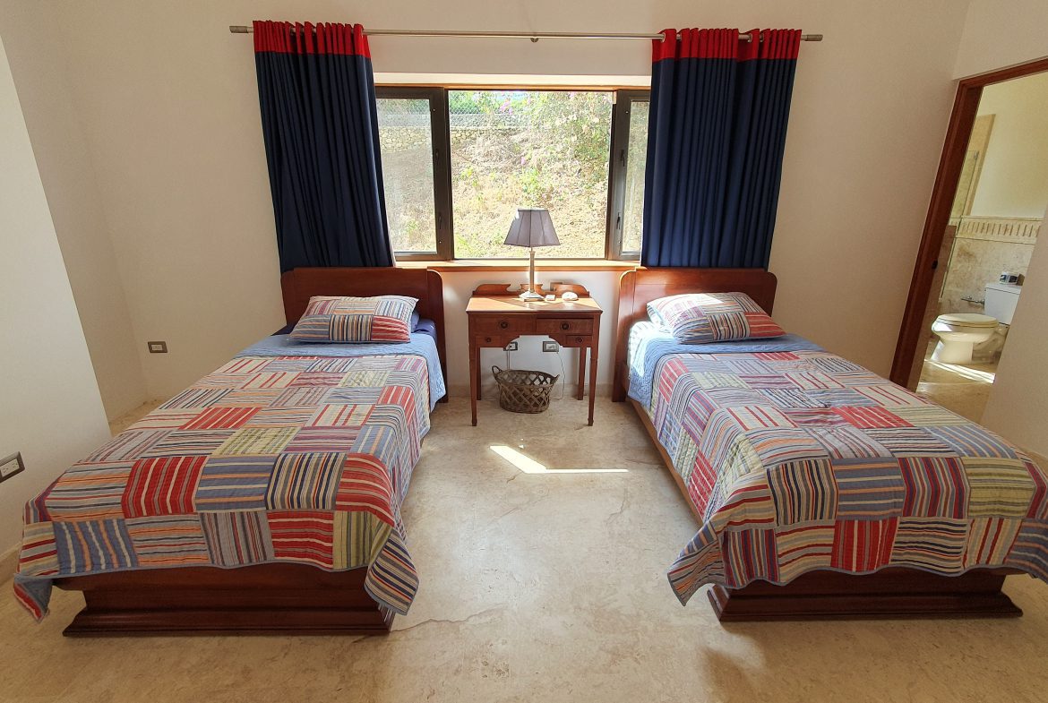 buyDRproperty Cozy guest bedroom with twin beds, patchwork quilts, and blue curtains. Sosua Real Estate