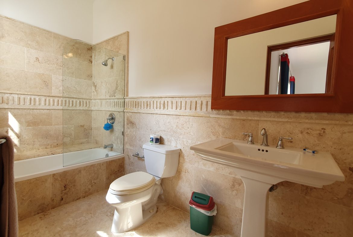 buyDRproperty Travertine tile bathroom with bathtub, pedestal sink, and mirror. Bathroom remodel. Sosua Real Estate