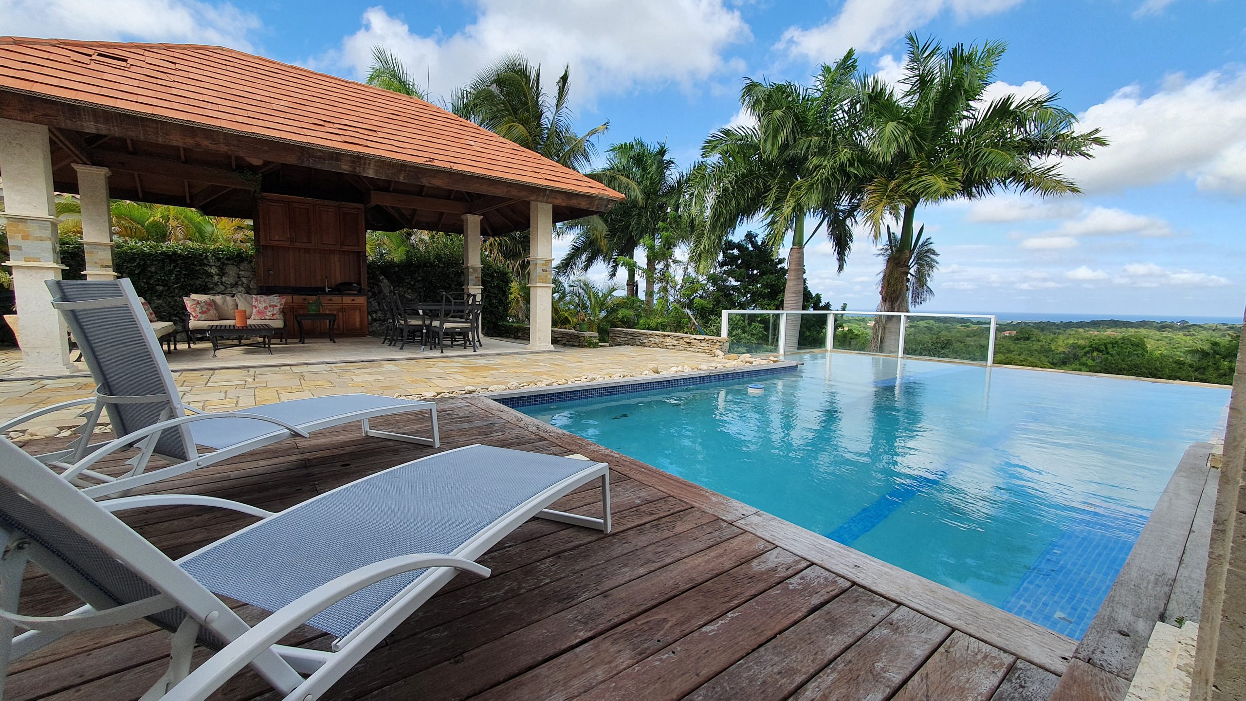 buyDRproperty Luxury villa with infinity pool, lounge chairs, and covered patio overlooking a tropical landscape. Sosua Real Estate