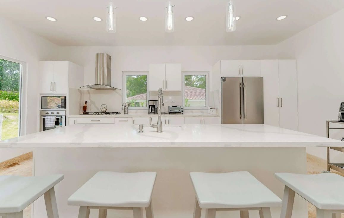 buyDRproperty Bright white kitchen with a large island, stainless steel appliances, and modern pendant lighting. Sosua Real Estate