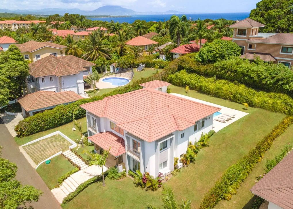 buyDRproperty Aerial view of a luxury villa with a red tile roof, swimming pool, and lush tropical landscaping. Sosua Real Estate