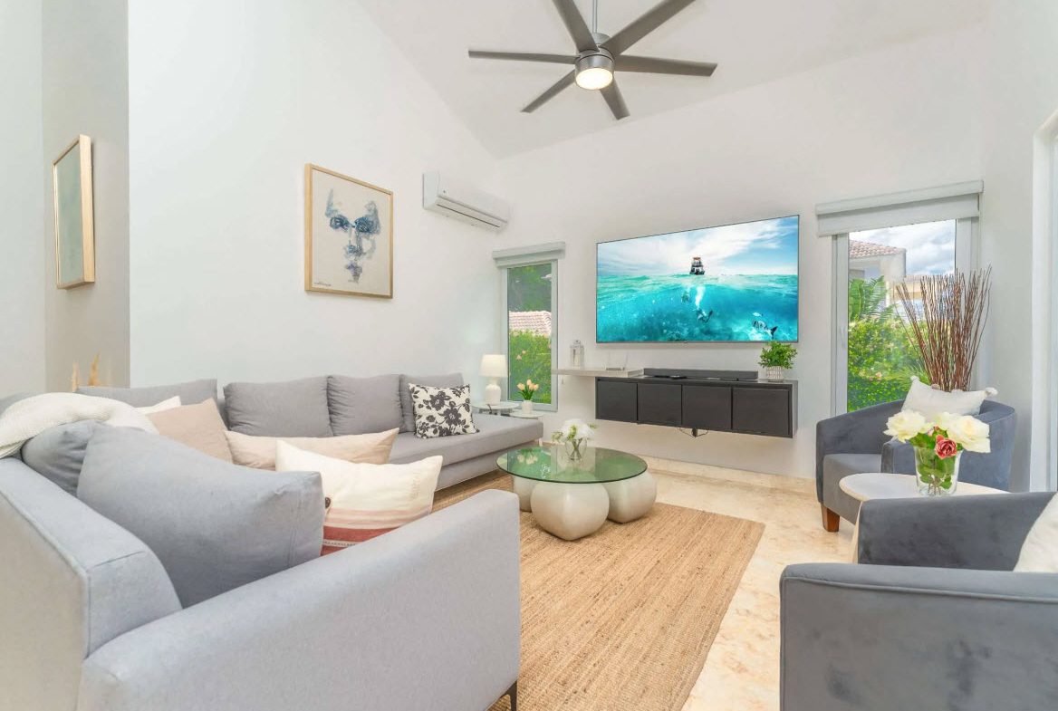 buyDRproperty Bright living room with gray sofa, TV, and beach scene art. Sosua Real Estate