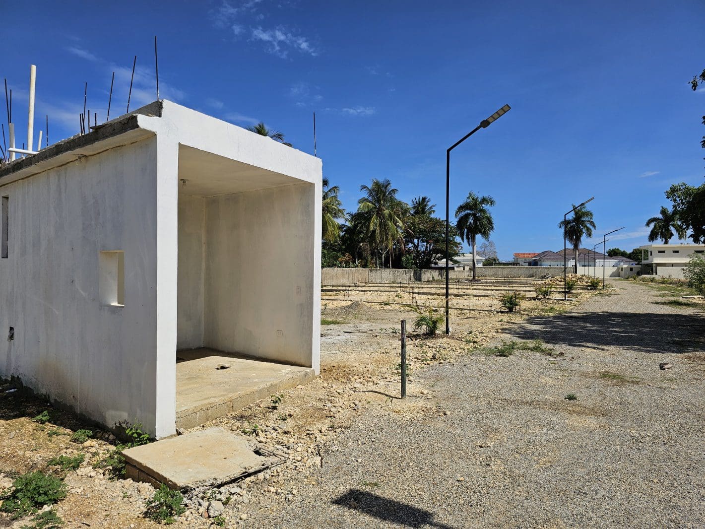 buyDRproperty Unfinished concrete structure on a sunny, empty lot with palm trees in the background. Sosua Real Estate