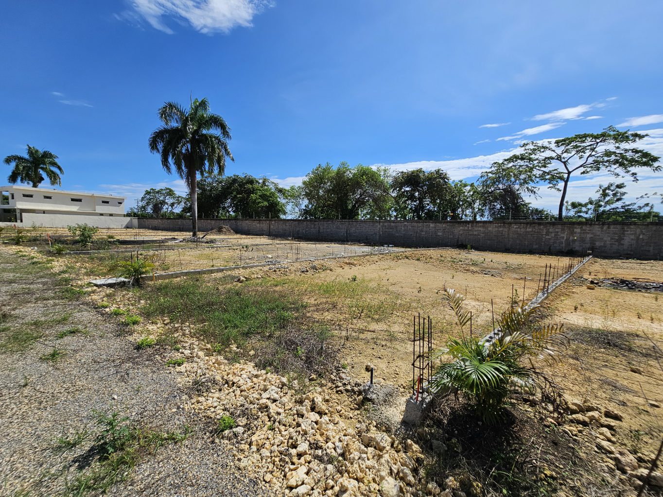 buyDRproperty Construction site with foundation work, palm trees, and blue sky. Sosua Real Estate