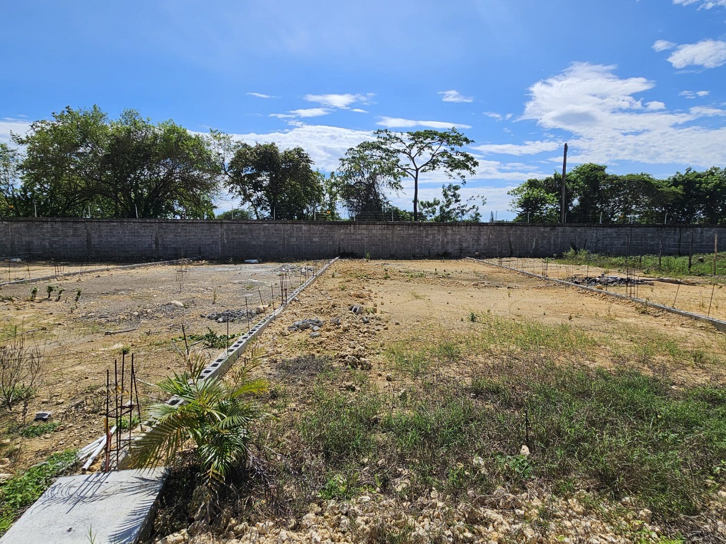 buyDRproperty Cleared land ready for construction, with a block wall in the background under a blue sky. Sosua Real Estate