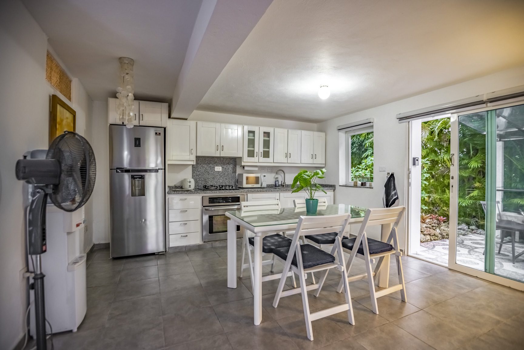 buyDRproperty Bright kitchen with white cabinets, stainless steel appliances, dining table, and a patio view. Sosua Real Estate