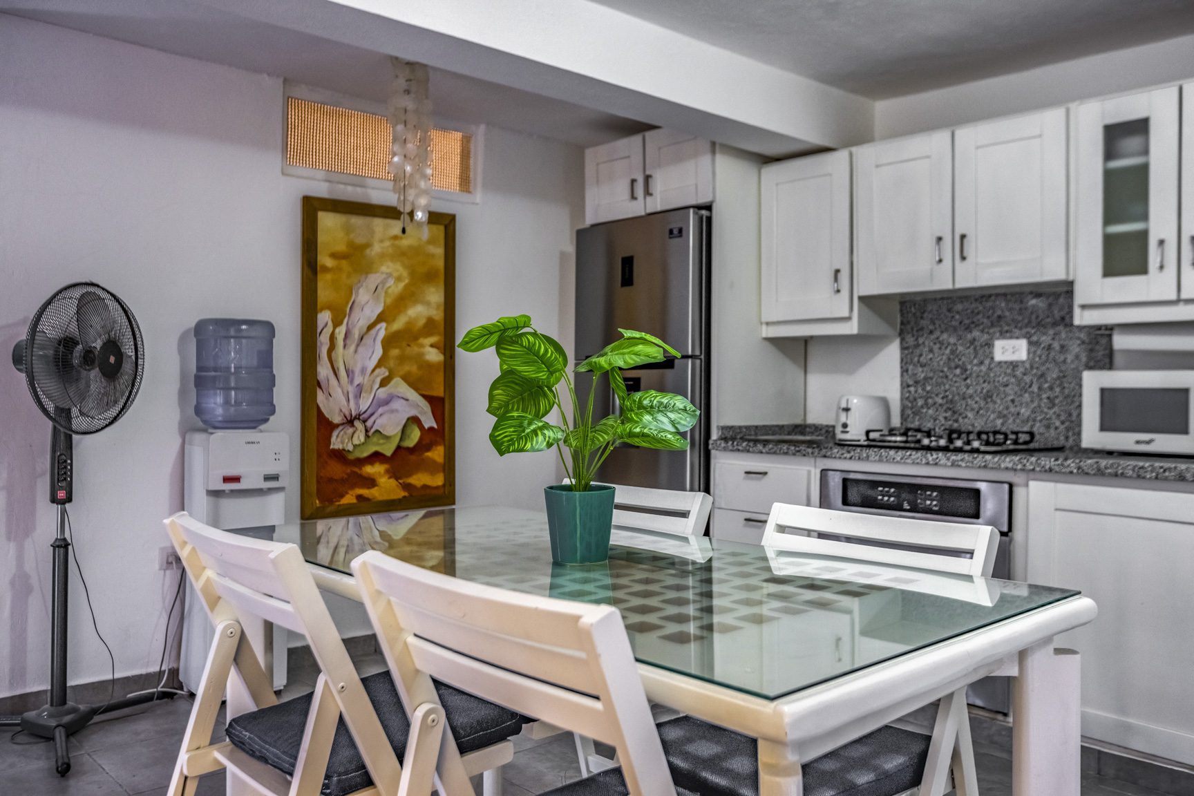 buyDRproperty Modern dining area with glass table, white chairs, and a plant centerpiece in a bright kitchen setting. Sosua Real Estate