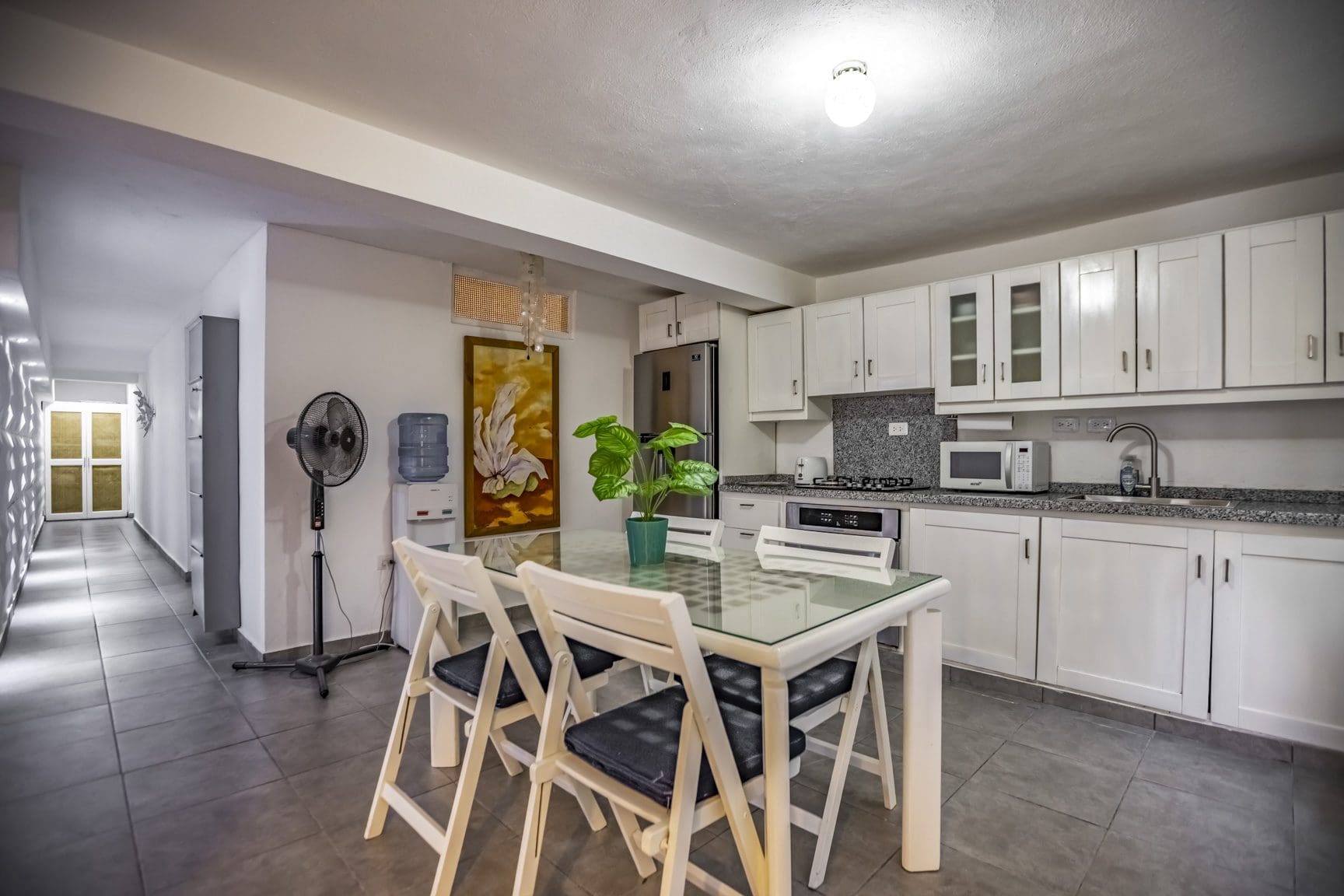 buyDRproperty Bright kitchen with white cabinets, a glass-top table, and a painting. Stainless steel appliances add a modern touch. Sosua Real Estate