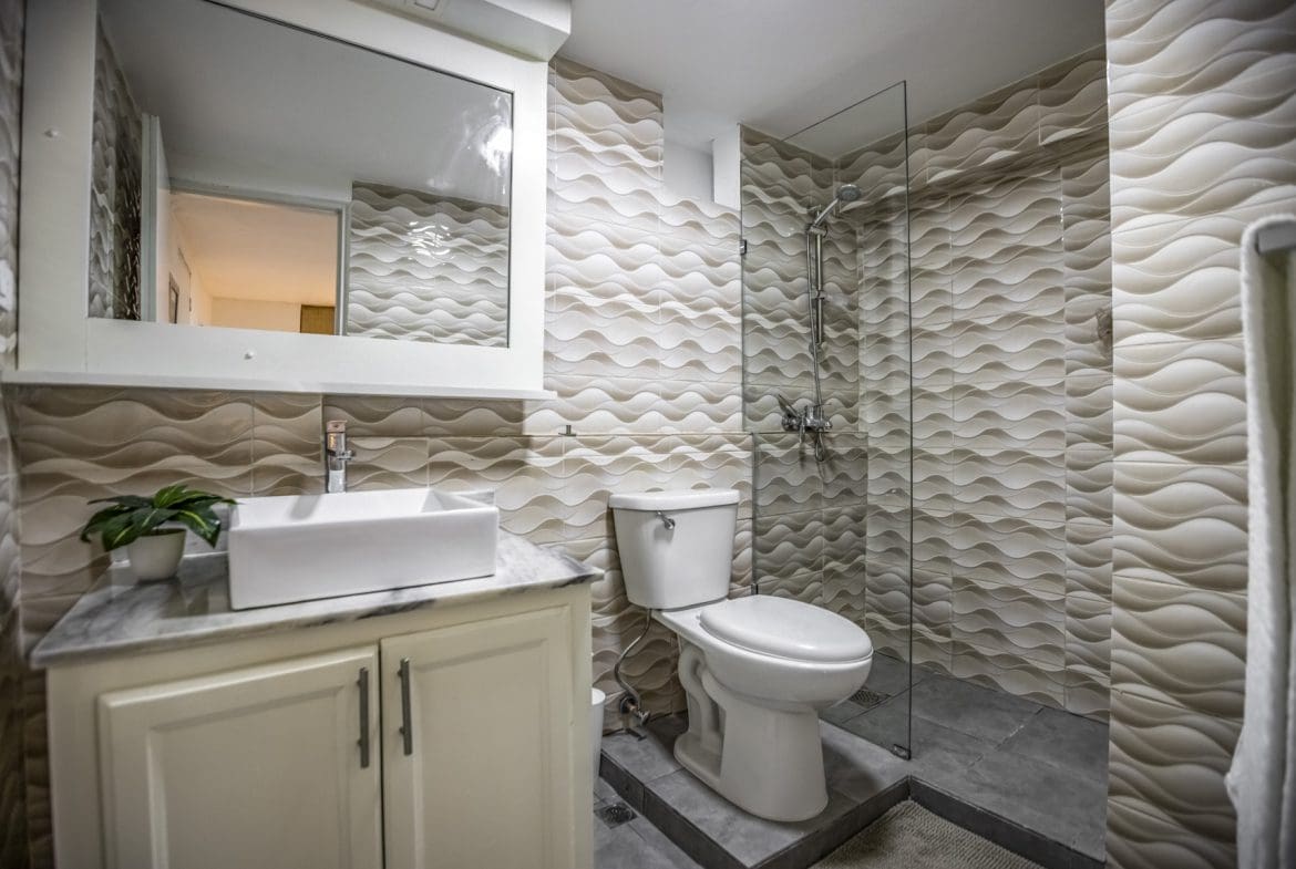 buyDRproperty Modern bathroom with textured beige walls, glass shower, and white vanity Sosua Real Estate
