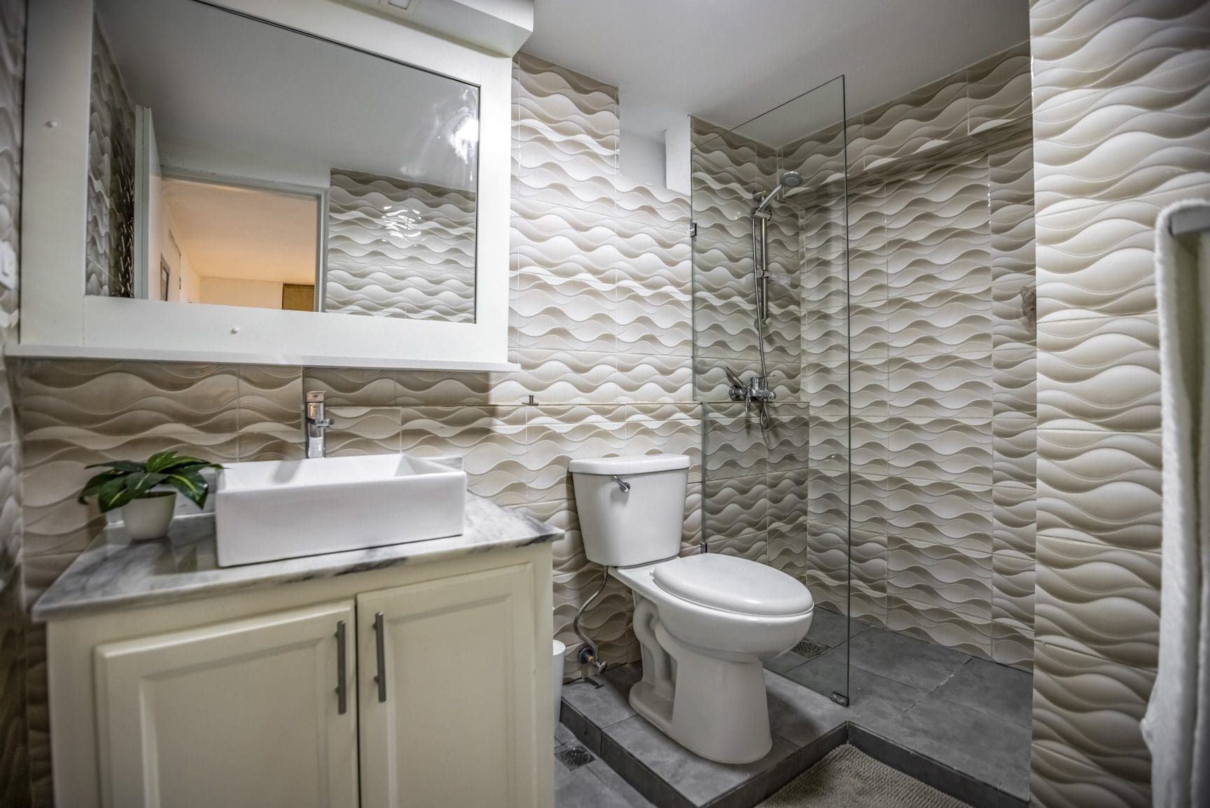 buyDRproperty Modern bathroom with textured beige walls, glass shower, and white vanity Sosua Real Estate