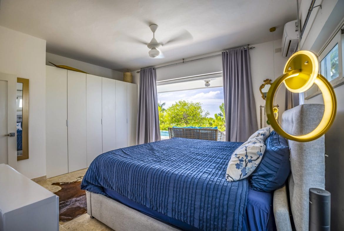buyDRproperty Bedroom with blue bedding, white wardrobe, and pool view Sosua Real Estate