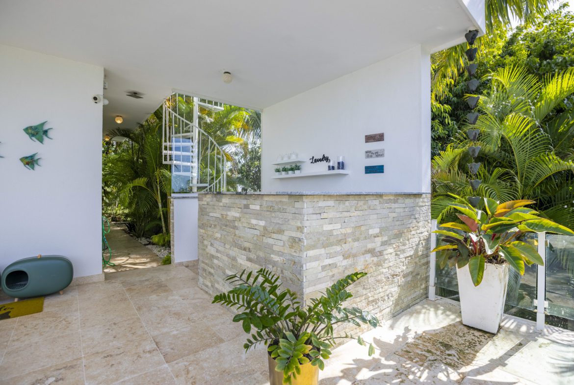 buyDRproperty Outdoor patio with white walls, stone accent, spiral staircase, and lush tropical plants. Sosua Real Estate