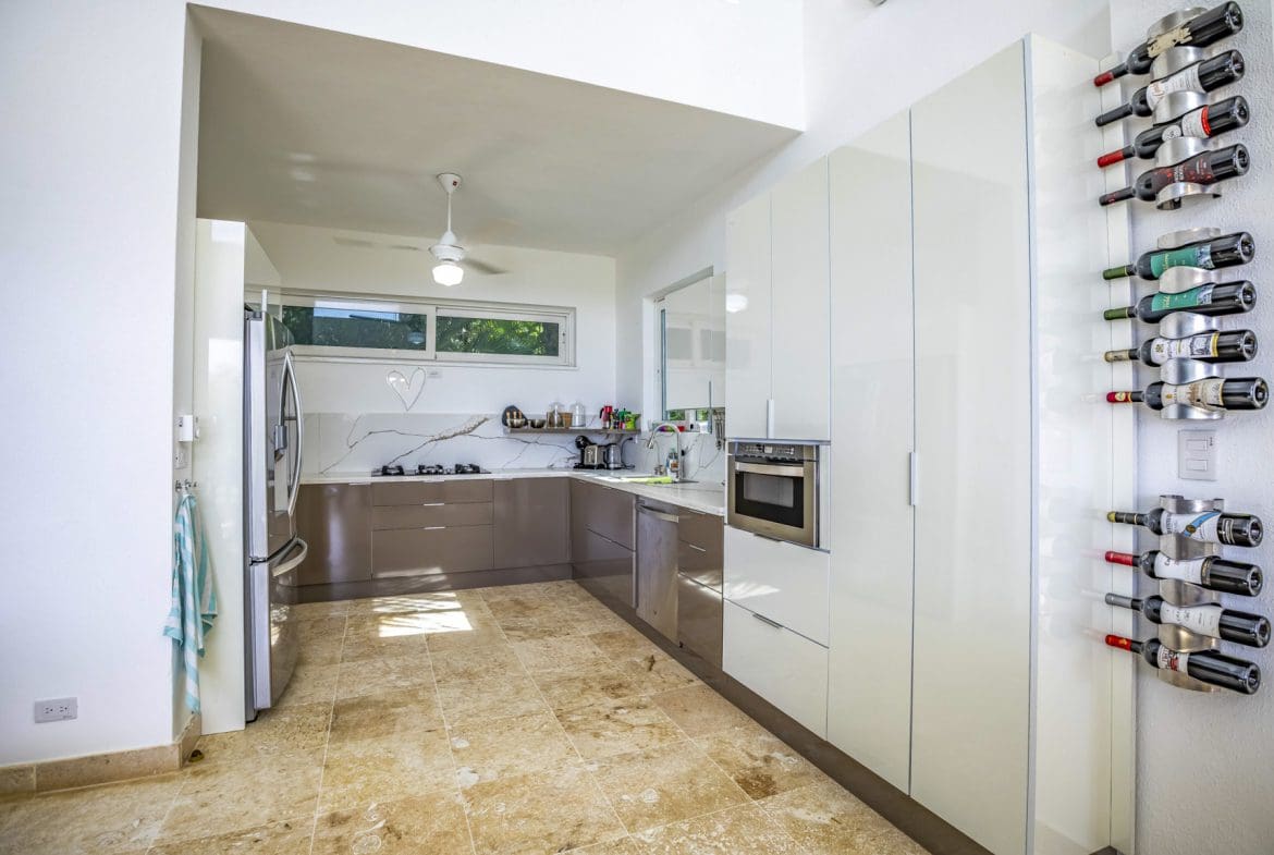 buyDRproperty Modern kitchen with travertine tile, white cabinets, and stylish wine rack. Sosua Real Estate