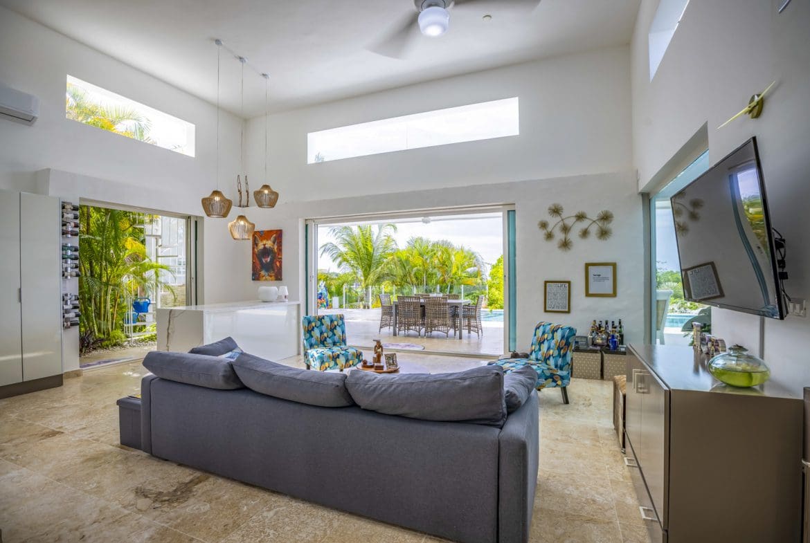 buyDRproperty Spacious living room with a large gray sofa, modern decor, and open access to patio garden Sosua Real Estate