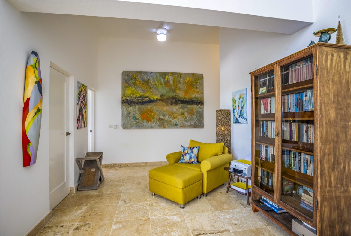 buyDRproperty Bright, eclectic entryway with yellow chaise lounge, colorful art, and a wooden bookcase. Sosua Real Estate