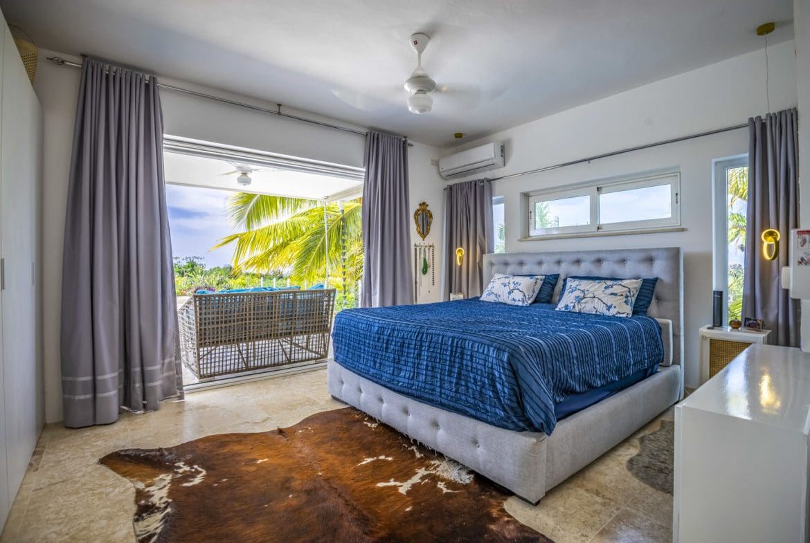 buyDRproperty Bright bedroom with blue bedding, balcony, and cowhide rug. Sosua Real Estate