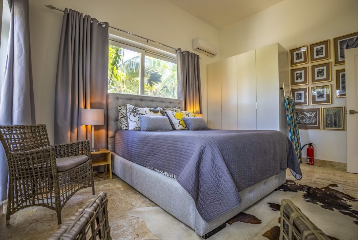 buyDRproperty Bright bedroom with gray bedding, wicker chairs, and framed art on the wall. Sosua Real Estate