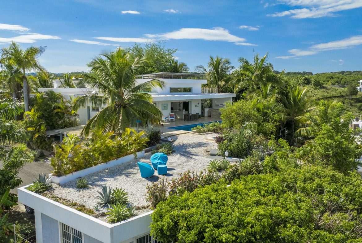 buyDRproperty Aerial view of a modern white villa with a rooftop garden, pool, and lush tropical landscaping. Sosua Real Estate