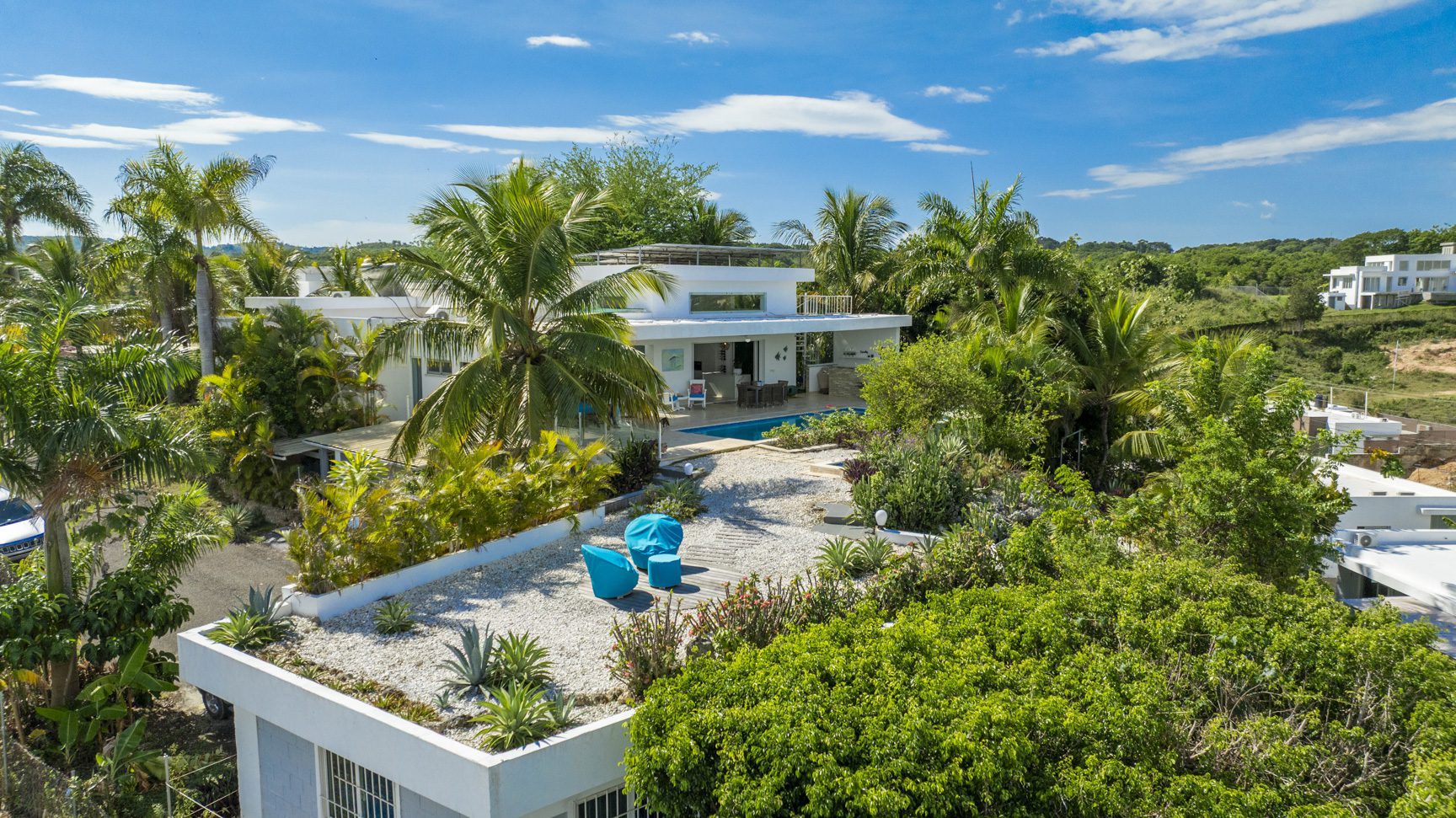 buyDRproperty Aerial view of a modern white villa with a rooftop garden, pool, and lush tropical landscaping. Sosua Real Estate