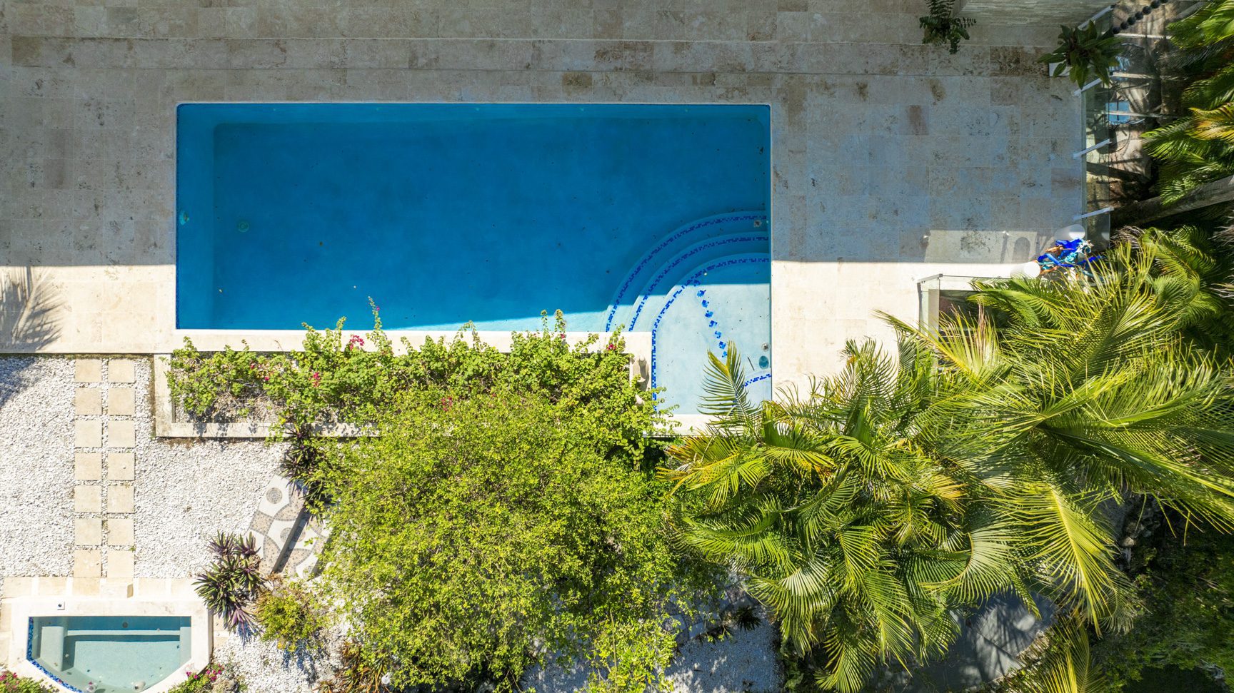 buyDRproperty Aerial view of a turquoise swimming pool surrounded by stone patio, lush greenery, and palm trees. Sosua Real Estate