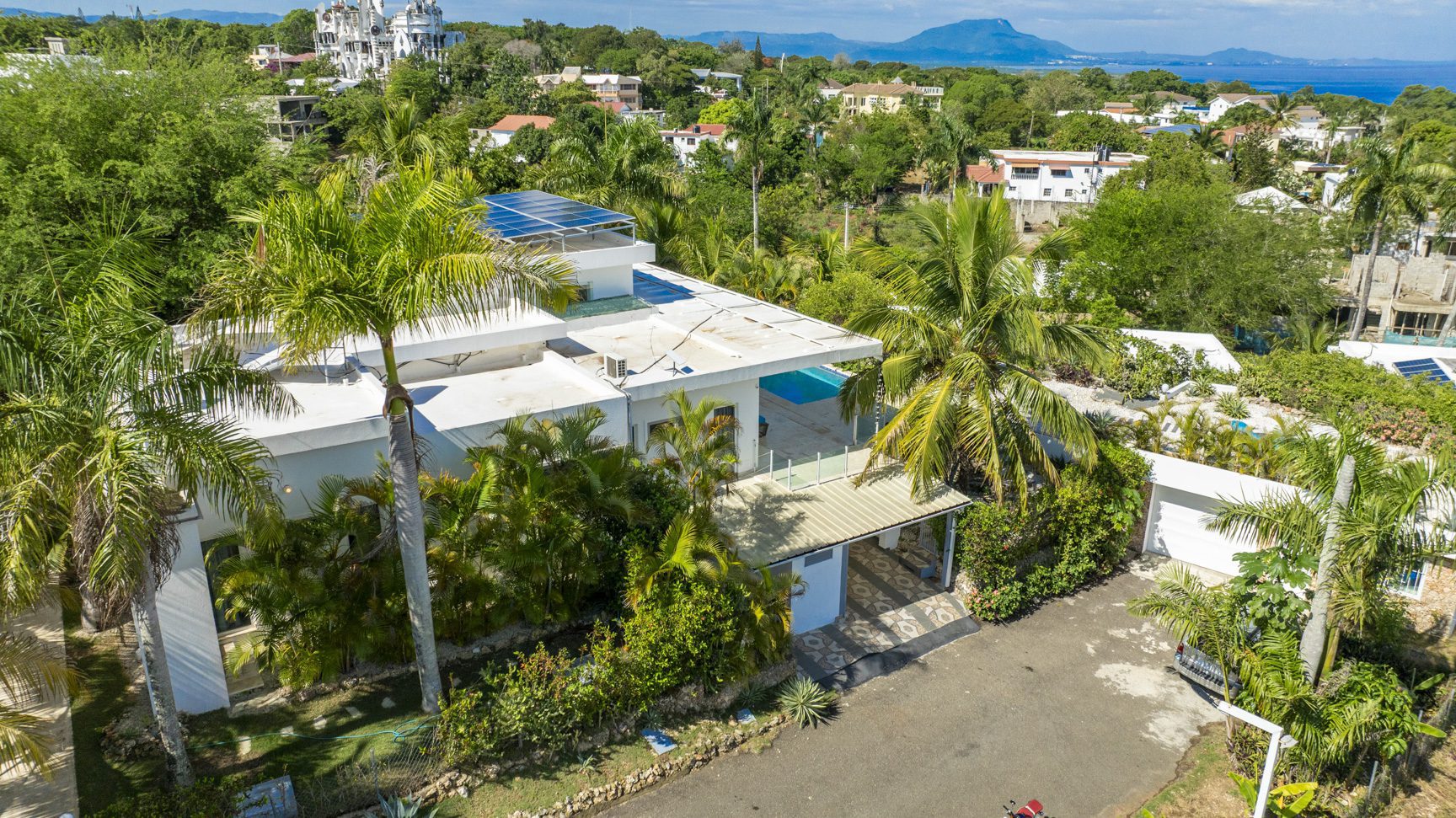 buyDRproperty Aerial view of a modern white villa with solar panels, surrounded by lush tropical greenery. Sosua Real Estate