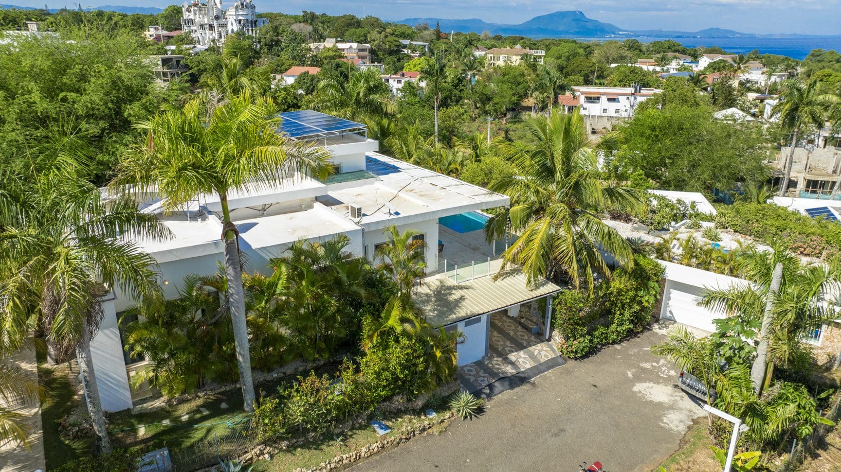 buyDRproperty Aerial view of a modern white villa with solar panels, surrounded by lush tropical greenery. Sosua Real Estate