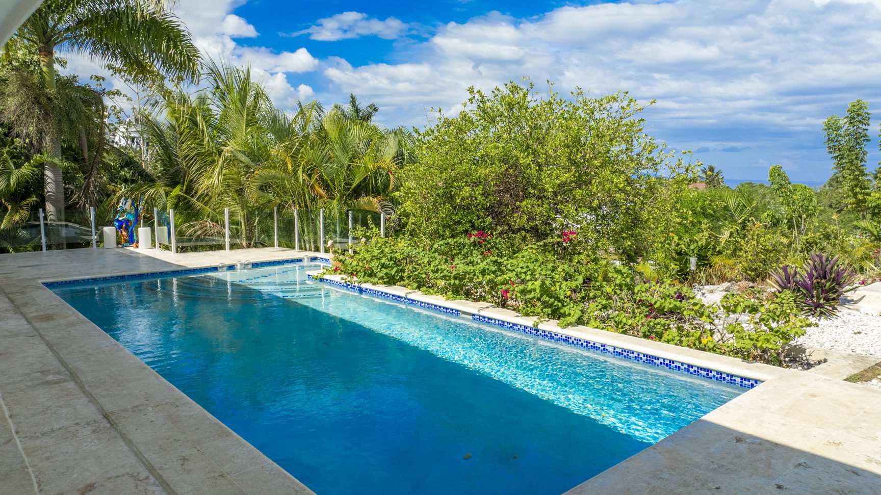 buyDRproperty Backyard swimming pool with clear blue water surrounded by lush greenery. Sosua Real Estate