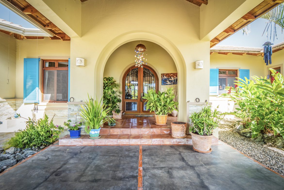 buyDRproperty Charming villa entrance with arched doorway and vibrant potted plants Sosua Real Estate