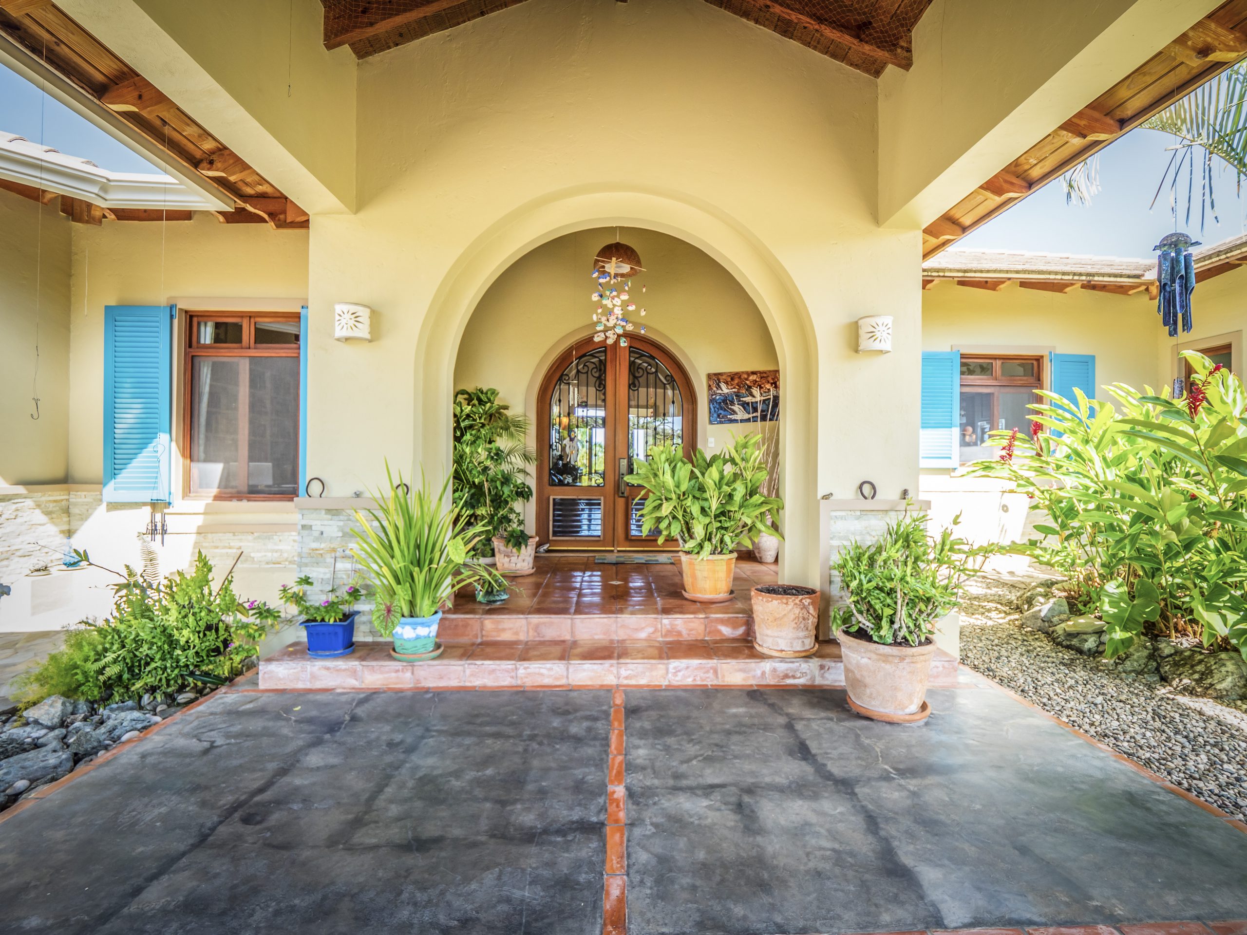 buyDRproperty Charming villa entrance with arched doorway and vibrant potted plants Sosua Real Estate