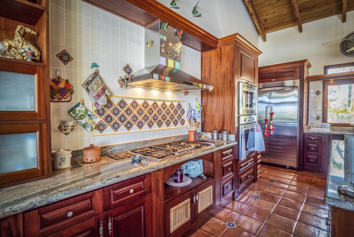 buyDRproperty Rustic kitchen with wooden cabinets, colorful backsplash, and stainless steel appliances Sosua Real Estate