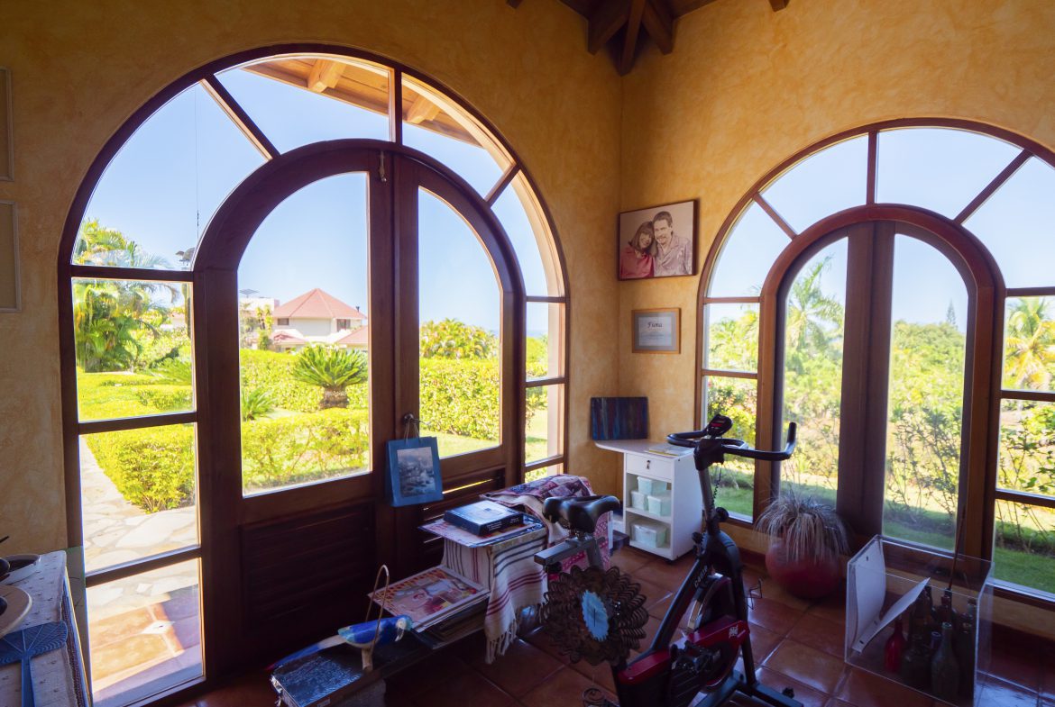 buyDRproperty Bright room with arched windows overlooking a garden and exercise bike inside Sosua Real Estate