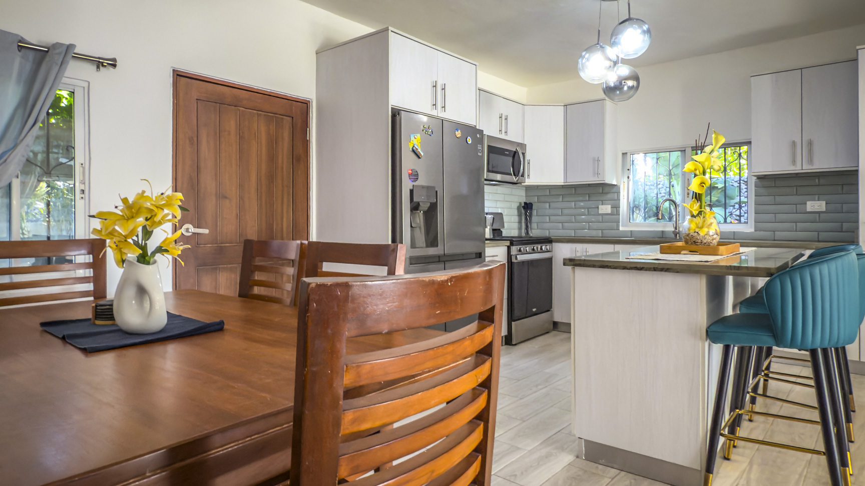 buyDRproperty Bright kitchen with wood dining table, yellow flowers, stainless steel fridge, and teal bar stools. Sosua Real Estate