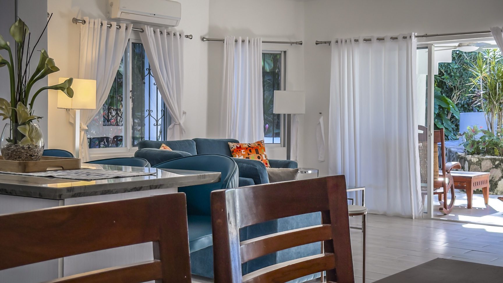buyDRproperty Bright living room with blue sofa, white curtains, and open patio door to a lush garden. Sosua Real Estate