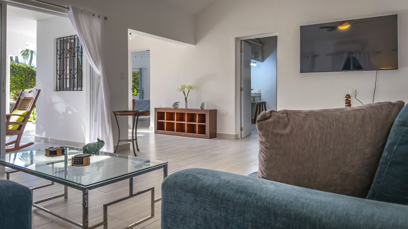 buyDRproperty Bright living room with a blue sofa, glass coffee table, and view of a sunny patio, creating a relaxing ambiance. Sosua Real Estate