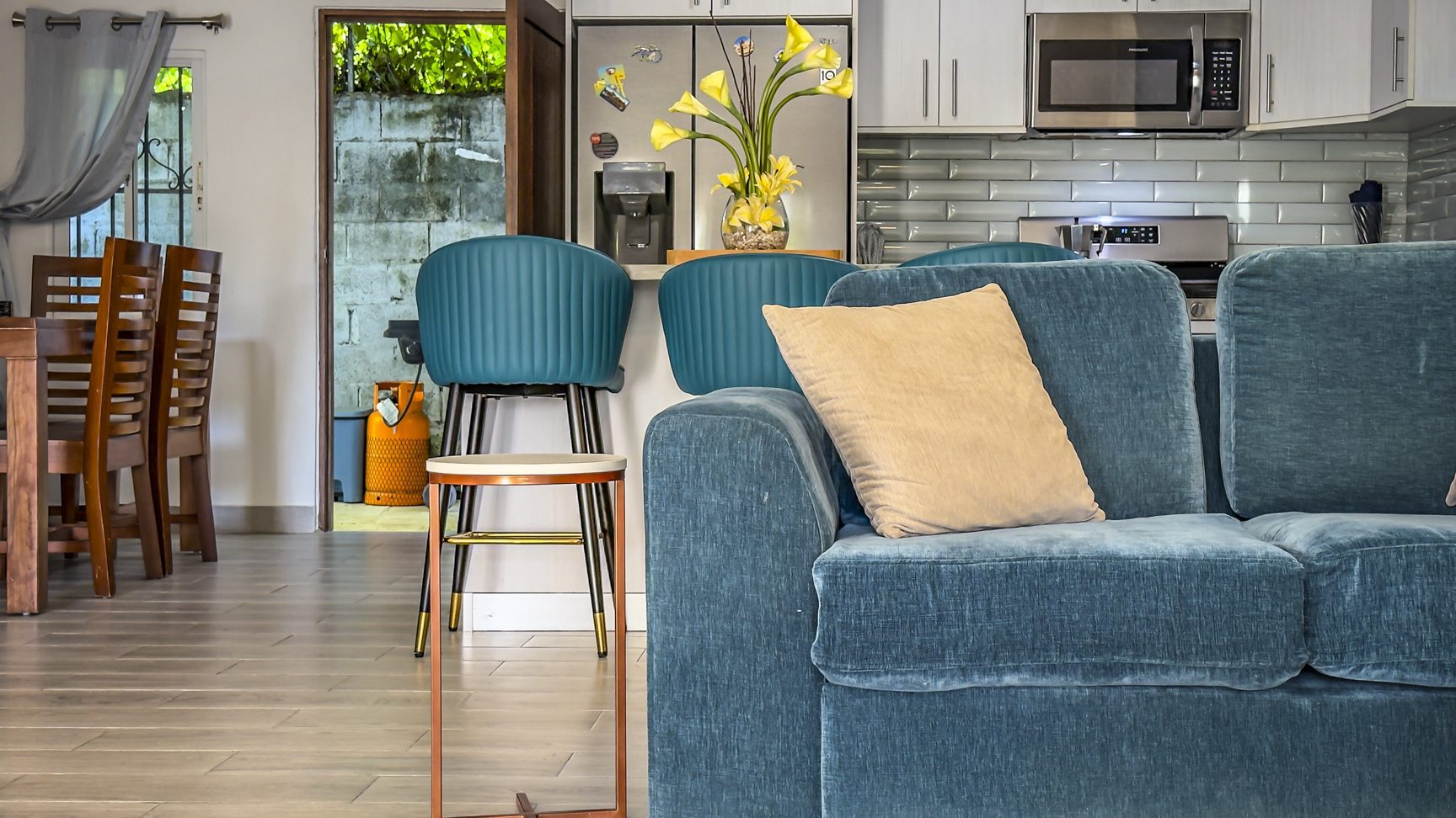 buyDRproperty Modern kitchen and living area with blue sofa, bar stools, and open doorway. Sosua Real Estate